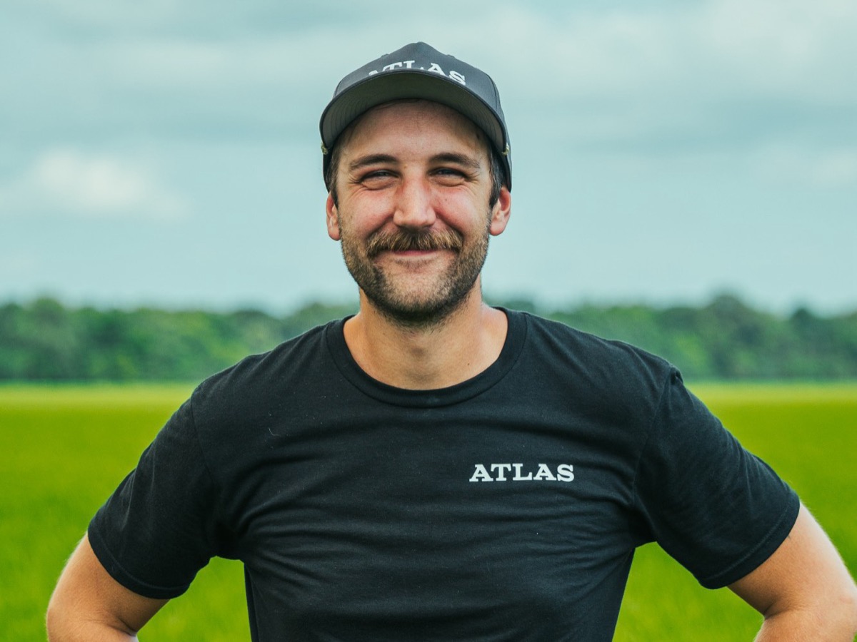 Clayton, smiling, hands on hips in a green field under a cloudy sky.