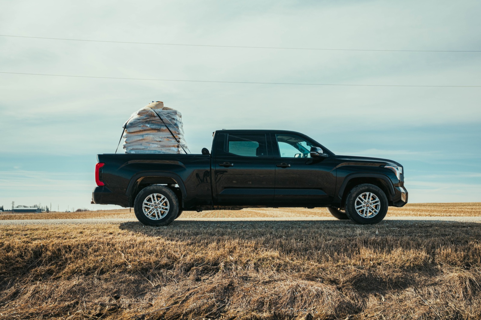 A pickup hauling a load of grain bags across open farmland.